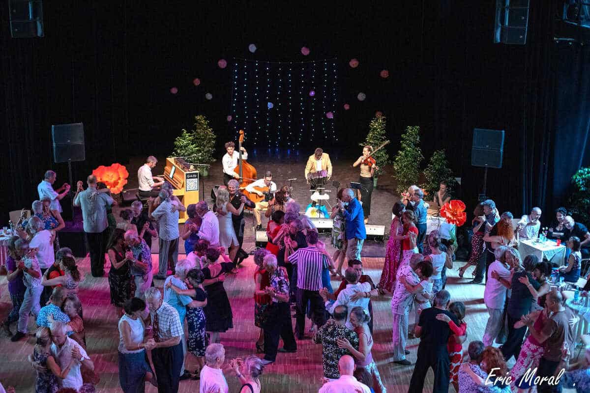 Les danseurs remplissent la piste pendant qu’un orchestre joue sur scène sous un décor lumineux.